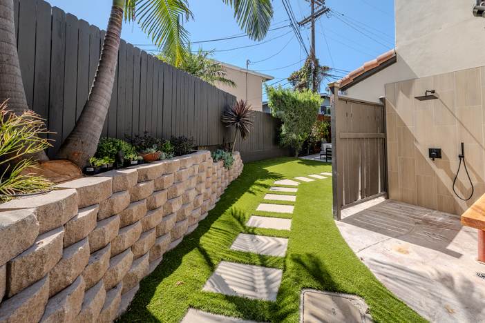Block retaining wall holding the grade above artificial turf and a paver stepping path.