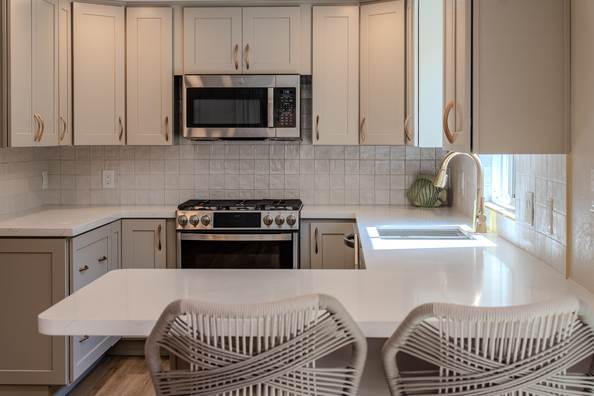 Kitchen run with pale shaker cabinets, quartz counters and brass tapware at the window.