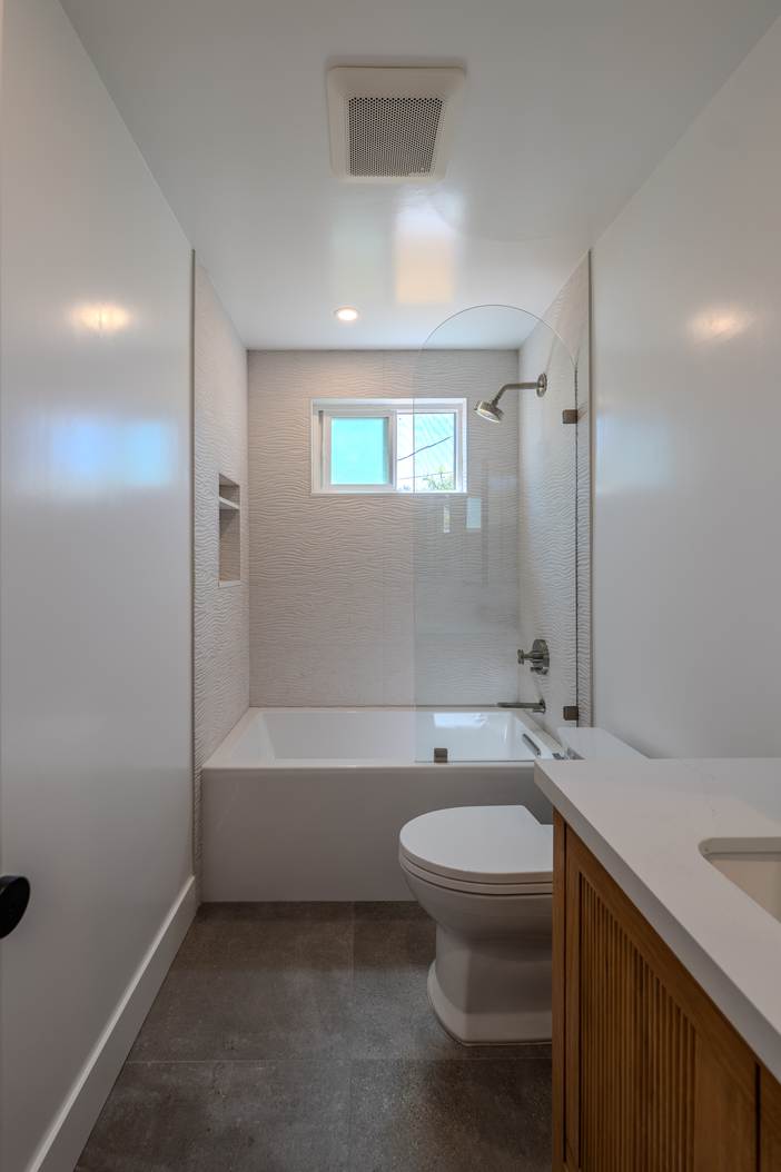 Bathroom with a shower over bath, stone tiled surround and a white oak vanity.