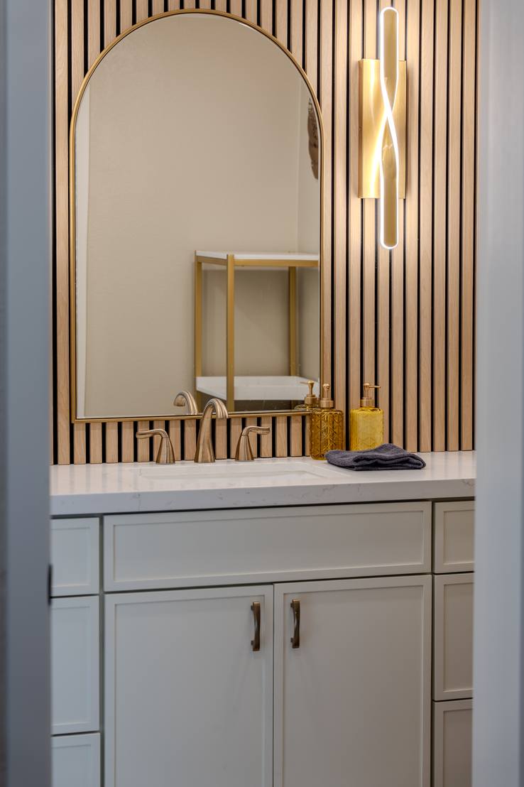 A finished bathroom vanity with an arched mirror set against a vertical wood slat wall, lit by slim sconces.