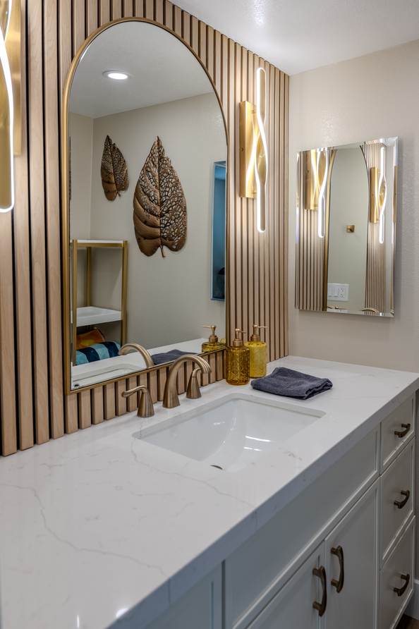 Bathroom vanity set against a vertical wood slat wall with an arched mirror.