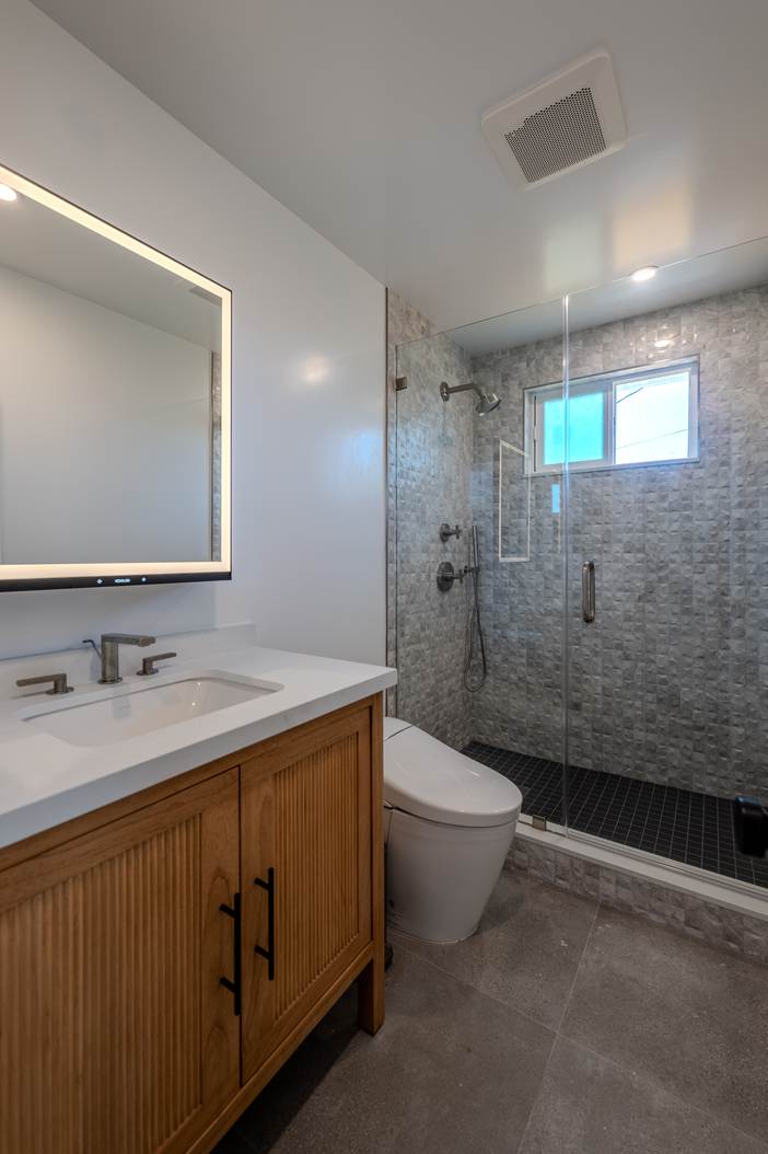 Bathroom with a double white oak vanity, backlit mirrors and a glass shower.