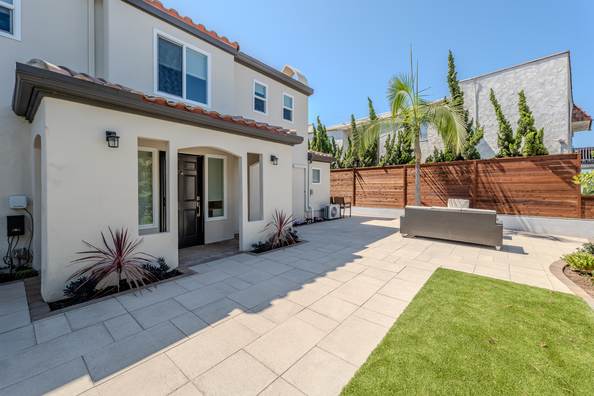Rear courtyard with large format gray pavers, a strip of lawn and a wood fence.