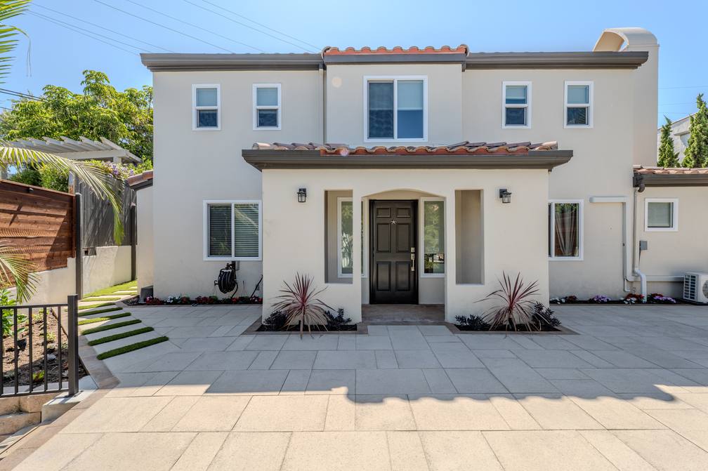The finished two story Spanish revival elevation at Escalones, with a tile roof, arched entry and paver forecourt.