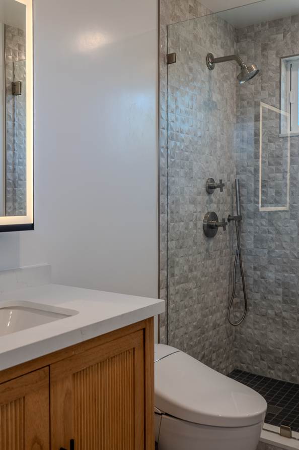 Second bathroom with a wood vanity, stone tiled shower and a glass enclosure.