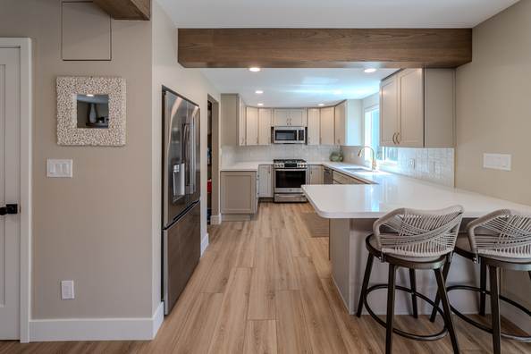 Kitchen with a waterfall island, bar stools, stainless appliances and pale cabinetry.