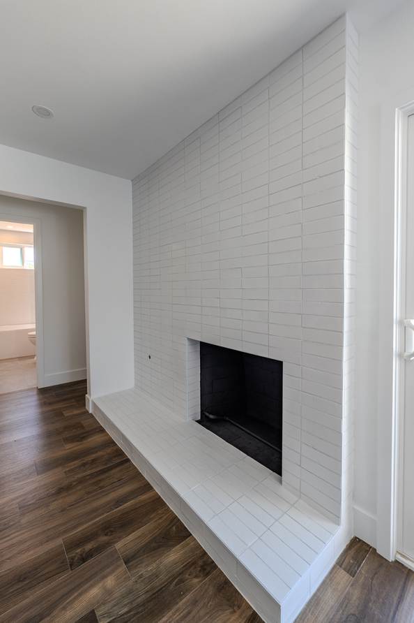 Interior living space with a floor to ceiling white tiled fireplace wall and wide plank floors.