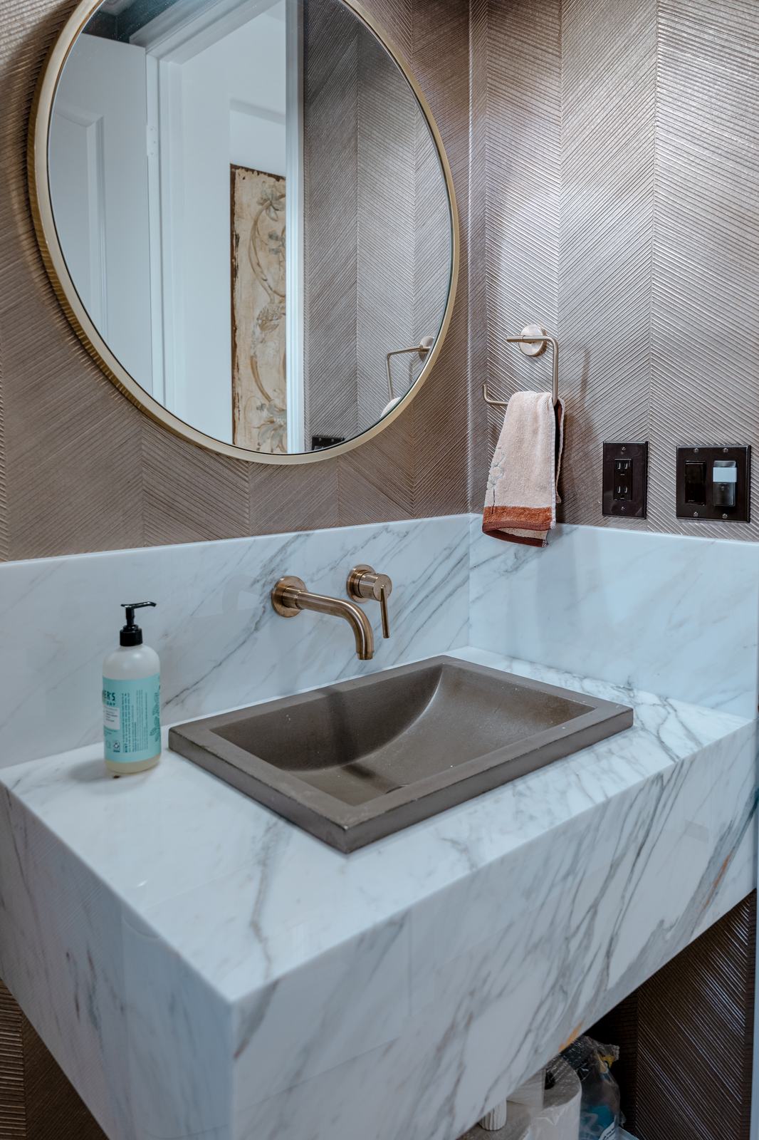 Mitred stone vanity with a wall mounted brass faucet and a round mirror