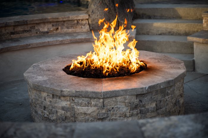 Fire pit in full flame at golden hour beside a pool