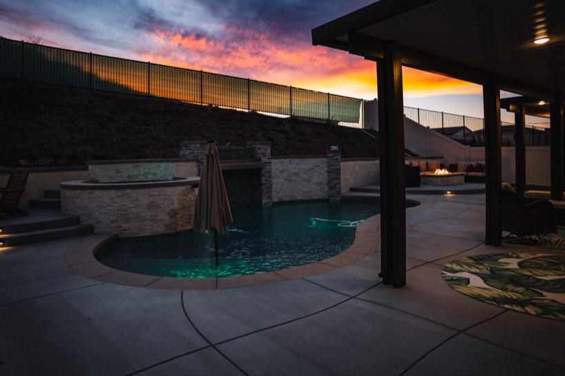 Freeform pool and spa under a blazing pink sunset with fire pit lounge