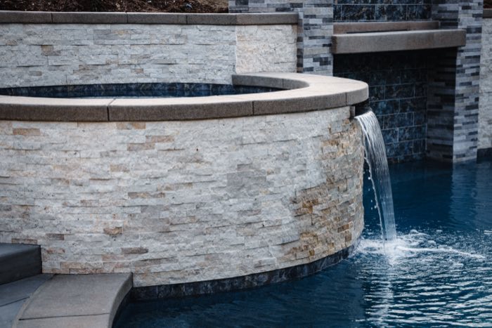 Spa spilling into a custom pool over a stacked-stone wall