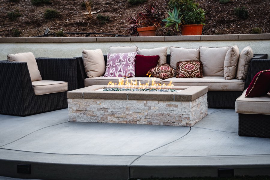 Fire pit lounge with sectional seating beside a lit pool at dusk
