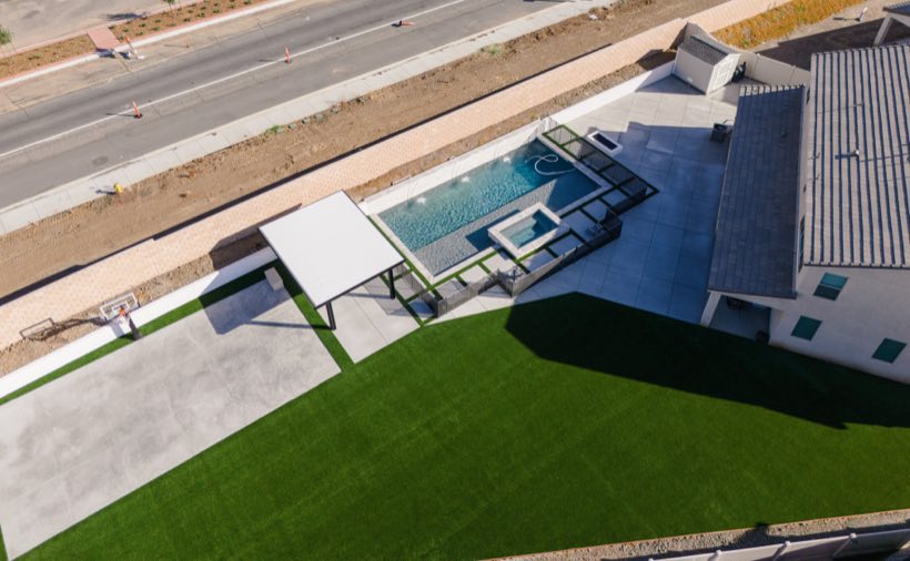 Aerial view of a modern geometric pool with automatic cover, turf and sport court