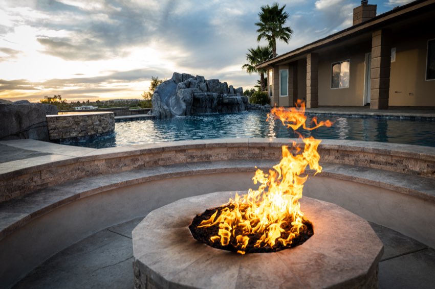 Fire pit burning beside a custom pool and rock waterfall at sunset