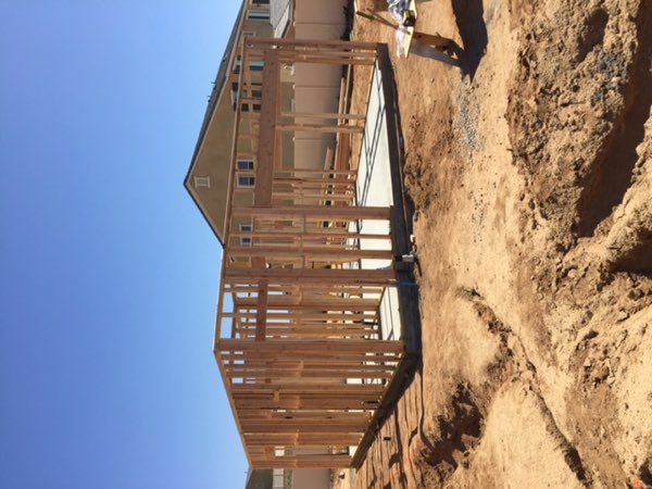 Stick framed walls standing open on the new slab with the existing two story house behind.