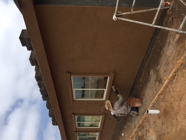A plasterer hand troweling brown coat stucco onto the wall below a finished window.