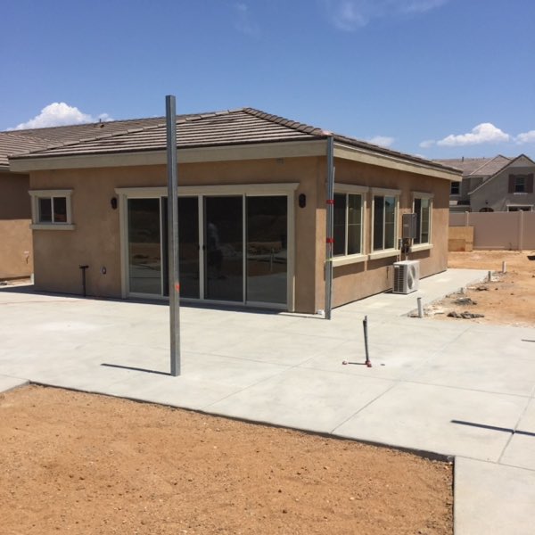 The finished addition with stucco, shingled roof, slider and windows, and a new poured concrete patio.