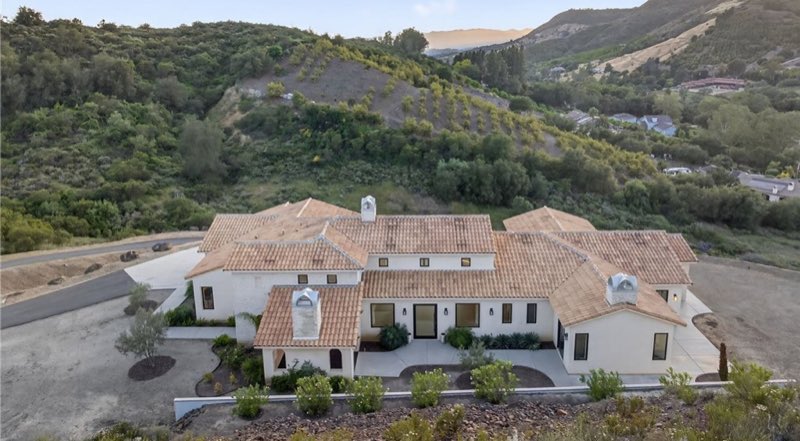 A finished custom home seen from above, tile roof and mature planting on a hillside lot.
