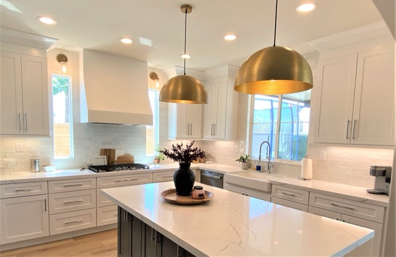 A finished kitchen with a large island, brass pendant lights and quartz counters.