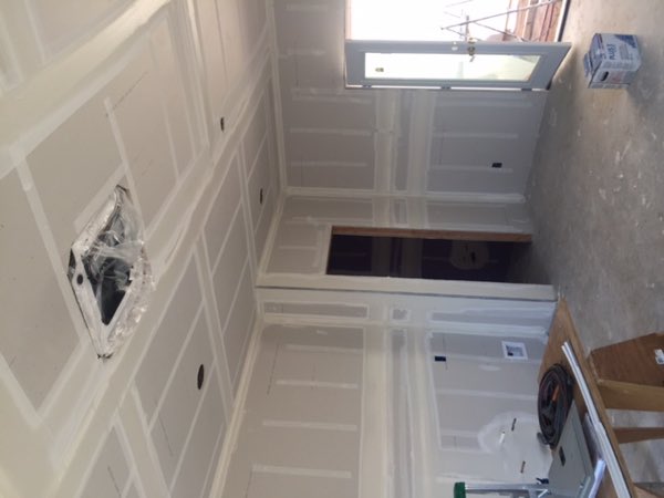 Interior with drywall hung and taped, ceiling finished, natural light through a doorway.