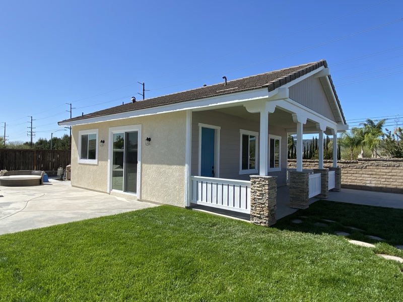 A finished detached ADU with a covered porch, lap siding and a lawn.
