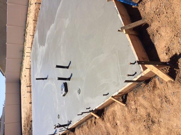 A freshly poured and troweled concrete slab with plumbing stub-ups, still inside its forms.