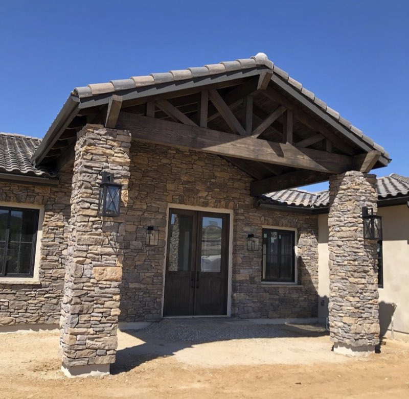 A finished custom home entry with stone columns and an exposed timber truss over the door.