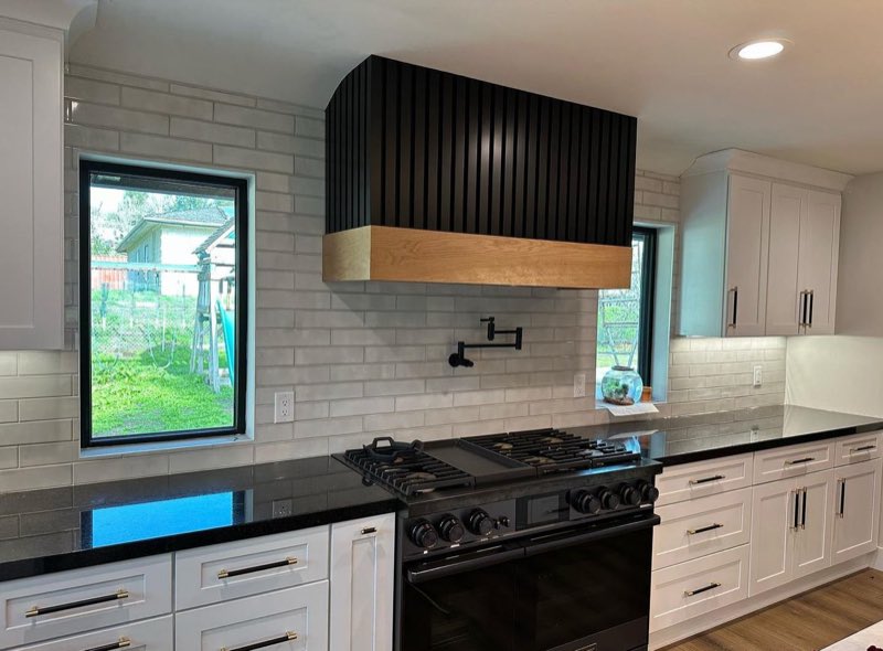 A finished kitchen with a custom hood, pot filler, stone counters and full height tile.